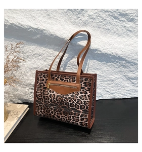 Detail of leopard print tote bag with brown leather handles and a front gold zipper pocket
