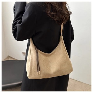 Macro detail of beige suede hobo bag featuring vertical stitching and braided tassel trim