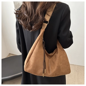 Dettaglio di una borsa hobo in camoscio marrone con tracolla larga indossata da modella