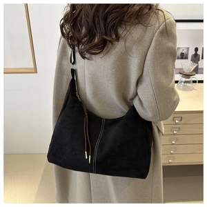 Detail of black suede tote bag with white stitching and brown tassel on model