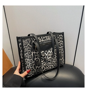 Detail of leopard print tote bag with black handles and front zipper pocket on a stool