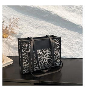 Detail of leopard print tote bag featuring black trim and long shoulder strap on a rock background