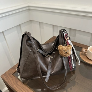 Retro dark brown matte leather tote bag with plush bear charm on a glass coffee table
