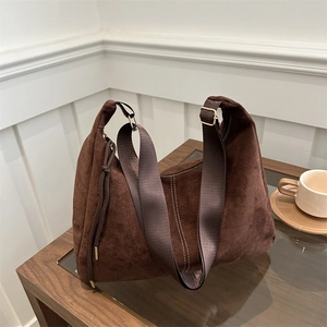 Borsa hobo in camoscio marrone scuro con tracolla larga su un tavolino in legno