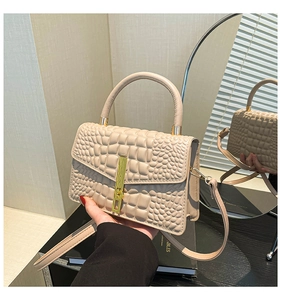 Close-up of beige crocodile pattern handbag with gold metal lock and leather handle