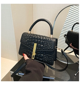 Detail of black crocodile texture bag featuring gold metal lock and leather handle