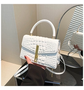 Detail of white crocodile embossed handbag featuring a long gold clasp and leather handle