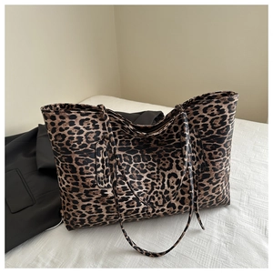Detail of leopard print tote bag on white bedding next to a stylish black blazer