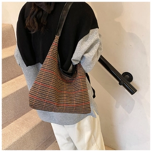 Detail of vintage plaid tote bag with black leather straps on a casual model outfit