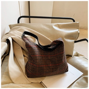 Close-up of a plaid pattern shoulder bag with black leather strap on a beige sofa