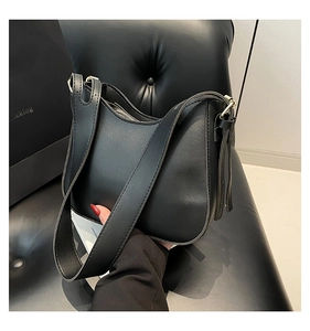Dettaglio di una borsa hobo in pelle lucida nera con tracolla larga su una sedia