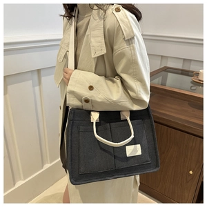Detailed view of canvas tote bag with two front pockets and white straps on a beige coat