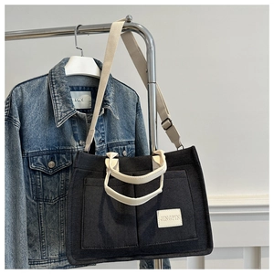 Detail of black canvas tote bag with contrast cream straps and dual front pockets