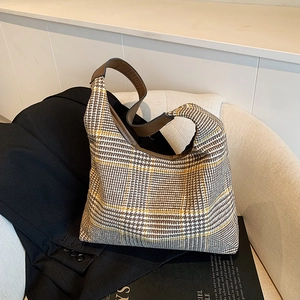 Classic houndstooth hobo bag with brown leather strap displayed on a beige armchair