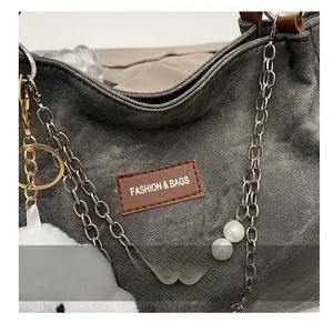Macro shot of dark grey canvas tote with leather label, pearl chain, and plush pendant