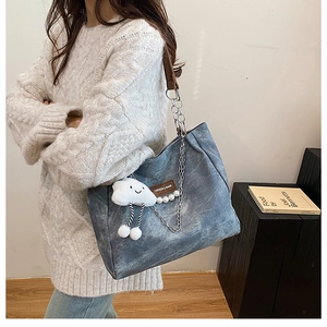 Detail of blue denim tote bag featuring chain straps and a plush cloud charm accessory