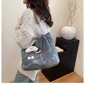 Blue canvas tote bag with leather handles and decorative pearl chain on model