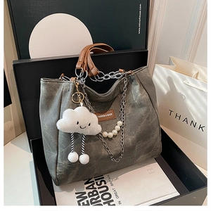 Detail view of grey tote bag with chain strap, pearl accent, and plush cloud charm