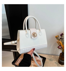 Detail der weißen Ledertasche mit Krokodilprägung und goldener Blumenschnalle