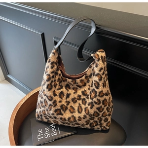 Detail of leopard print plush tote bag with black leather strap on a stool