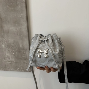 Silver bow-accented pleated bucket bag with metallic finish and drawstring strap
