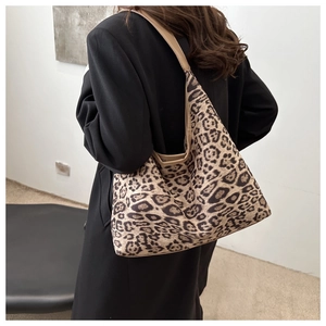 Sac cabas léopard porté à l'épaule sur un manteau noir dans un intérieur minimaliste