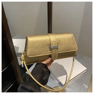 Close-up of golden crocodile pattern shoulder bag with silver buckle held by a hand