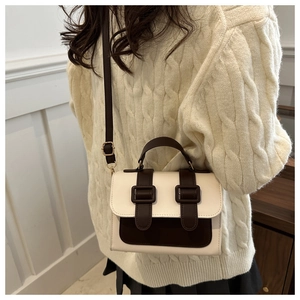 Detail of color-block satchel with double straps worn over a cream cable knit sweater