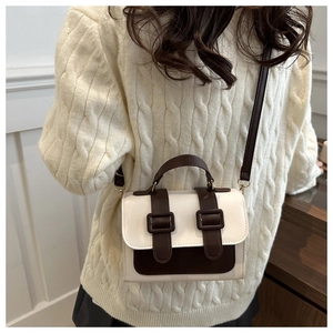 Detail of a vintage-style color-block crossbody bag styled with a beige cable-knit sweater