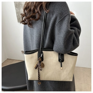 Dettaglio della grande borsa tote in pelle bianco sporco con tracolla nera e ciondolo