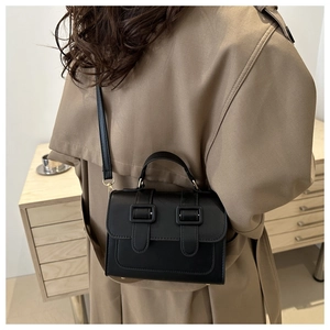Fashionable black square bag worn with khaki trench coat in a minimalist setting
