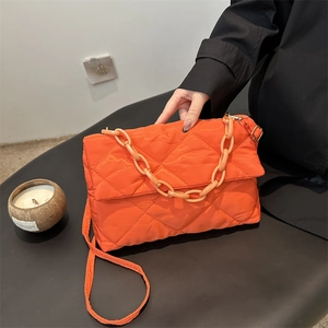 Sac bandoulière matelassé orange avec chaîne épaisse et sangle sur un canapé sombre