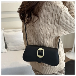 Detail of minimalist black baguette bag with textured gold buckle worn by model
