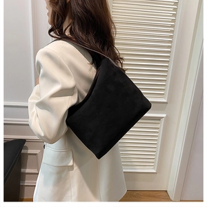 Sac seau chic en daim noir avec bandoulière marron porté sur un blazer blanc