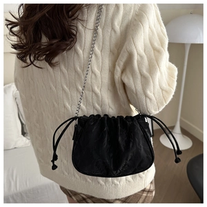 Detail of black pleated cloud bucket bag with silver chain strap on a model shoulder