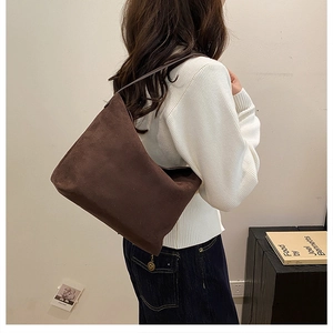 Détail d'un sac cabas demi-lune en daim marron foncé porté par un mannequin en décor