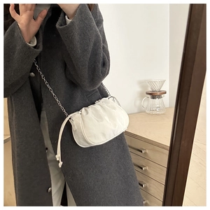 Detail of white pleated dumpling bag with silver chain strap on grey wool coat