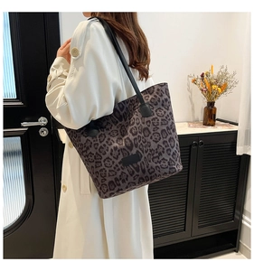 Leopard print tote bag with black leather handles shown on shoulder for size context