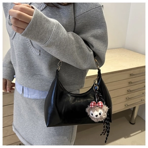 Close-up of black oil wax leather crescent bag with a cute plush bear charm detail