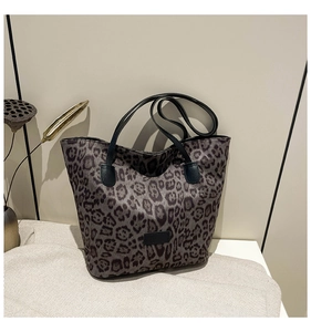 Detail view of leopard print tote bag with dark leather handles on textured fabric