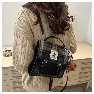 Detail of plaid backpack with leather straps and a brown teddy bear plush charm