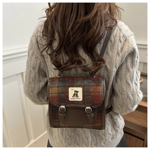 Detail of vintage plaid wool backpack featuring cute bear embroidery and leather straps