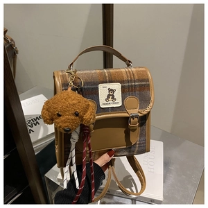 Detail of vintage plaid backpack featuring brown leather trim and cute teddy bear charm