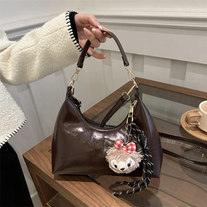 Dark brown oil-wax leather crescent bag with gold buckle and plush charm detail