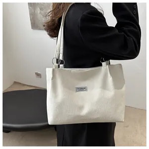 Detailed view of white corduroy tote bag with metallic rings and fashion logo patch