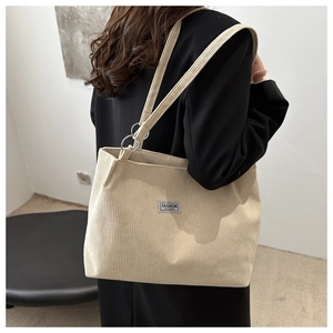 Detail of beige corduroy tote bag showing metal ring buckle and fashion instinct label