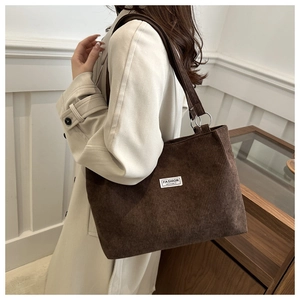 Macro detail of dark brown corduroy tote bag featuring an embroidered fashion label tag