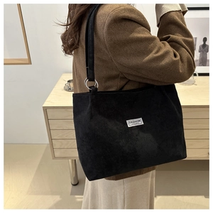 Close-up of black corduroy tote bag with metal rings and fashion label on a model