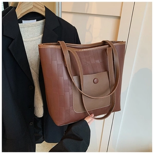 Detail of a large brown tote bag with woven texture and a front leather pocket with button