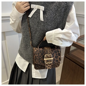 Détail du sac bandoulière léopard avec boucle dorée porté par un mannequin chic